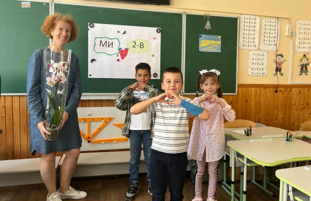 Three children bring flowers to their teacher which is traditional on the first day of school.